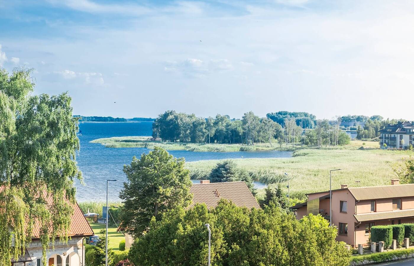 Widok na nadmorską wieś z domami z dachówek, bujną zielenią, trzcinowym brzegiem i spokojną zatoką idealną na relaks.