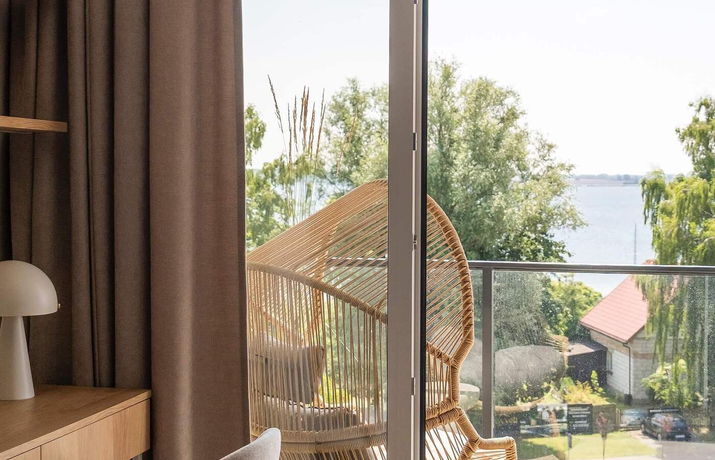 Pokój z balkonem: pleciony fotel rattanowy, szklana balustrada i widok na jezioro, biurko z lampą