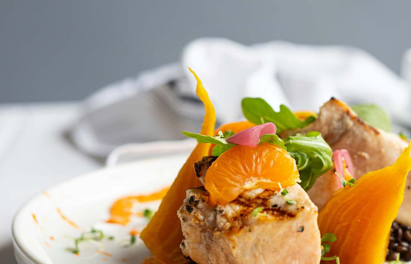 Grillowane kawałki ryby na pomarańczowym sosie z cząstką mandarynki, pieczonymi złocistymi burakami, mikrozieleniną i marynowaną cebulką.