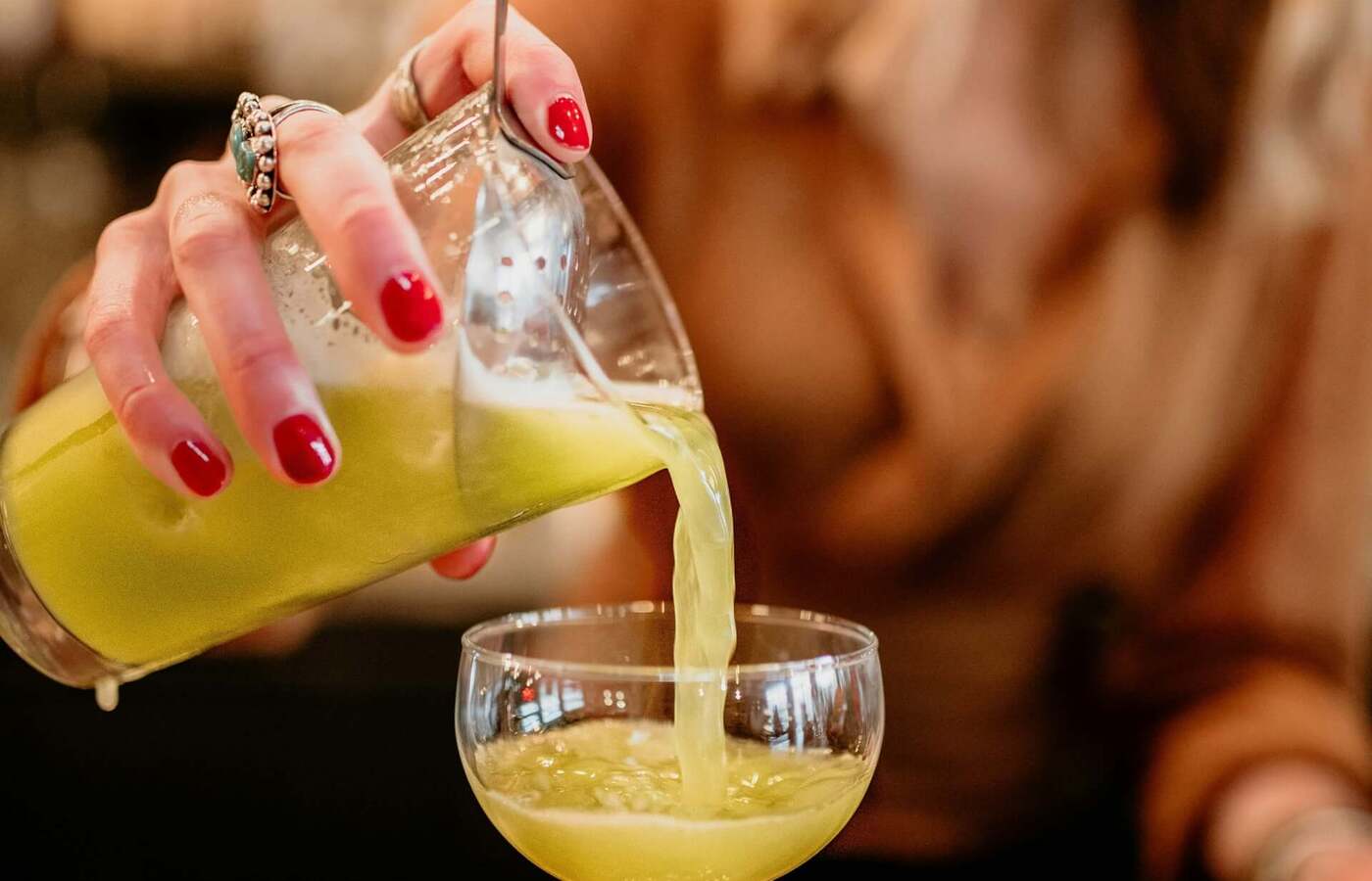 Barmanka z czerwonym lakierem nalewa jasnozielony koktajl do kieliszka coupe w przytulnym, rustykalnym barze hotelowym.