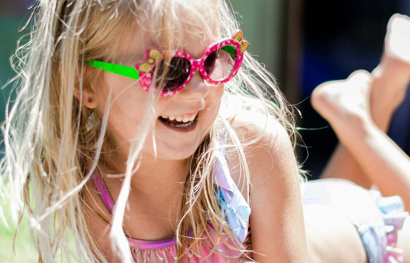 Dziewczynka w kostiumie i kolorowych okularach leży na słonecznym tarasie, zajadając przekąski przy basenie