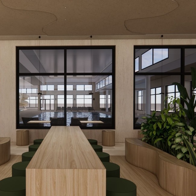 Długi drewniany stół wspólny z zielonymi stołkami, donicami z roślinami i dużymi oknami z widokiem na jasny kryty basen z leżakami i zjeżdżalnią.