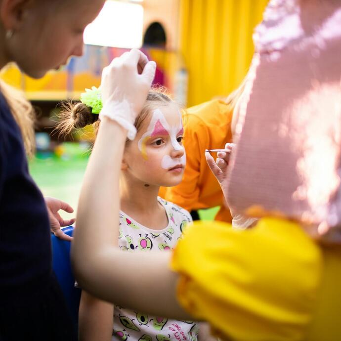 Animator maluje dziewczynce twarz w kolorowej strefie zabaw hotelu, rodzinna atmosfera.