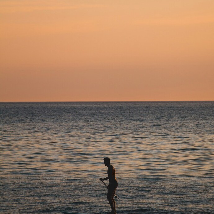 Sylwetka osoby na desce do paddleboardingu na spokojnym morzu podczas złotego zachodu słońca