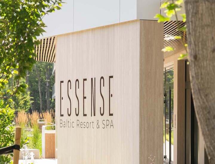Wejście z logo 'ESSENSE Baltic Resort & SPA' na nowoczesnej kamiennej elewacji, z ogrodem i fontanną.