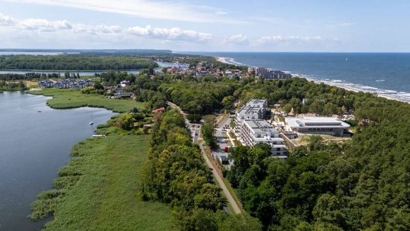 Nadmorski kurort z nowoczesnymi białymi budynkami hotelowymi między lasem, laguną i piaszczystą plażą, widok na morze.