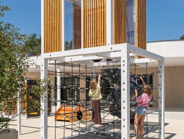 Nowoczesne patio hotelowe z drewnianą pawiloną i białą konstrukcją linową, na której bawią się dwoje dzieci