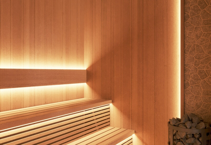 Drewniana sauna spa z kilkupoziomowymi ławkami, ciepłym podświetleniem LED i piecem z kamieniami do relaksu.