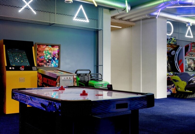 Hotelowa sala gier ze stołem do air hockeya, retro automatami, samochodzikiem dla dzieci i kolorowymi neonami na suficie