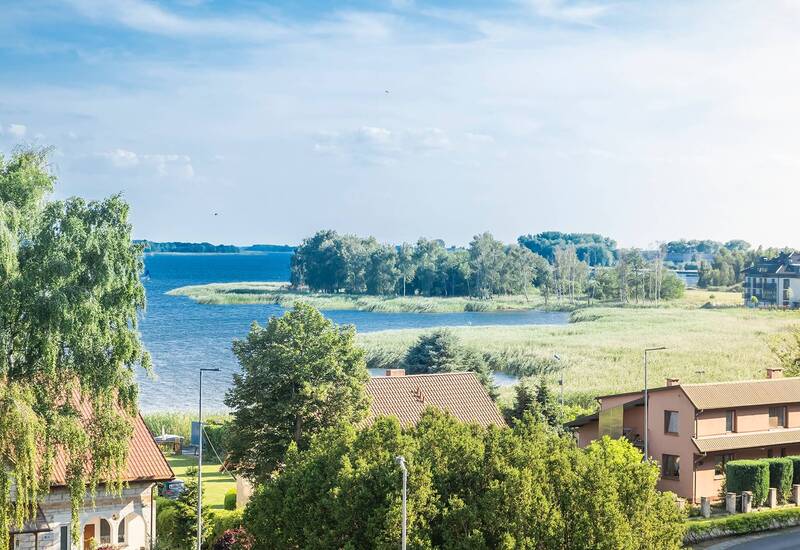 Widok na nadmorską wieś z domami z dachówek, bujną zielenią, trzcinowym brzegiem i spokojną zatoką idealną na relaks.