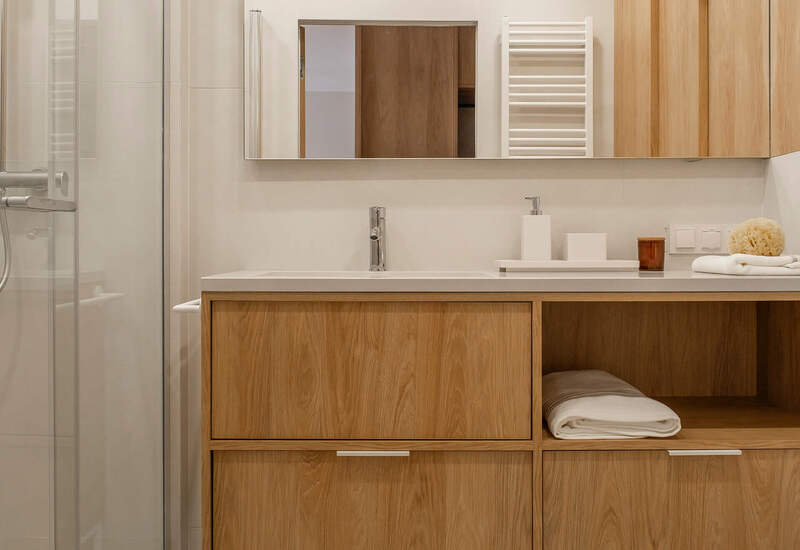 Nowoczesna łazienka hotelowa z drewnianą szafką, dużym lustrem, szklanym prysznicem, wieszakiem na ręczniki i złożonymi ręcznikami.