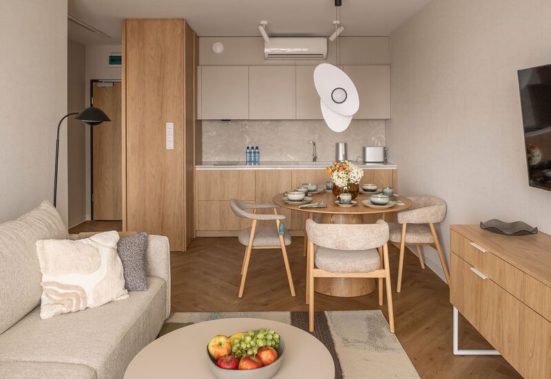 Nowoczesne studio z drewnianą kuchnią, okrągłym stołem dla czterech, wygodną sofą, telewizorem, wiszącą lampą i miską świeżych owoców