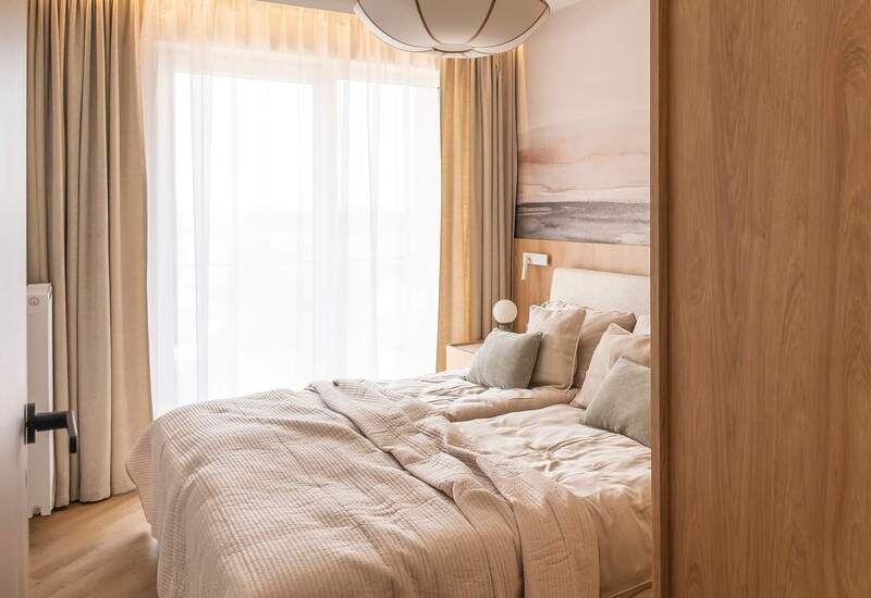 Jasny, przytulny pokój z dużym łóżkiem, miękką neutralną pościelą, lampką nocną, drewnianą boazerią i zasłonami od podłogi do sufitu