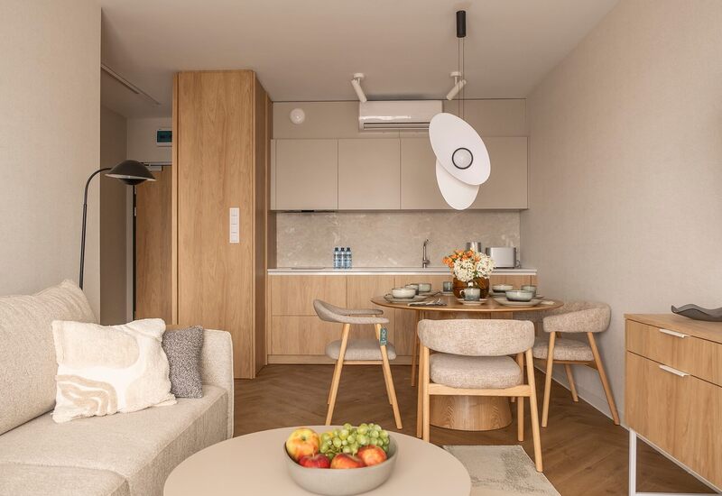 Nowoczesne studio z aneksem kuchennym, okrągłym stołem na cztery, przytulną sofą, miską owoców i drewnianymi wykończeniami.