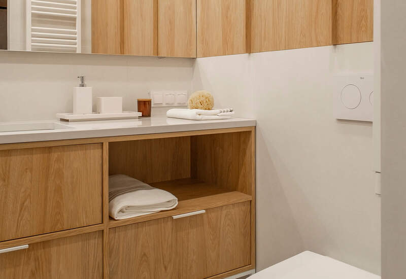 Nowoczesna łazienka z drewnianą szafką, wiszącą toaletą, białym blatem, ręcznikami i dozownikiem mydła