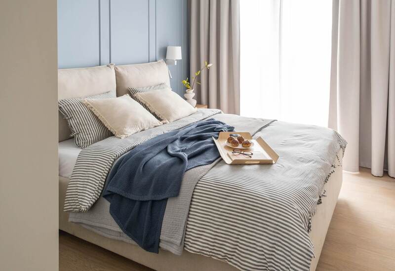 Przytulne duże łóżko z pasiastą pościelą, warstwowymi narzutami, tacą ze śniadaniem i zwiewnymi zasłonami