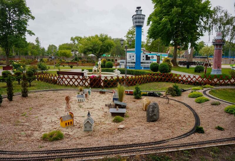 Miniaturowa plenerowa wioska z modelowymi torami, dekoracyjną fontanną i niebieską wieżą w zadbanym parku.