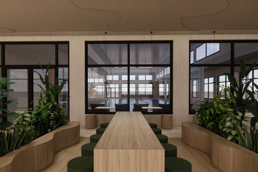 Długi drewniany stół wspólny z zielonymi stołkami, donicami z roślinami i dużymi oknami z widokiem na jasny kryty basen z leżakami i zjeżdżalnią.