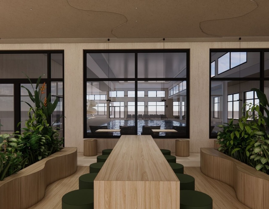 Długi drewniany stół wspólny z zielonymi stołkami, donicami z roślinami i dużymi oknami z widokiem na jasny kryty basen z leżakami i zjeżdżalnią.