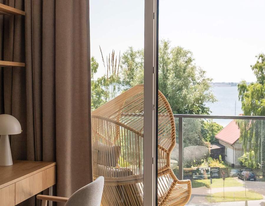 Jasny pokój z biurkiem i lampą, balkon z wiklinowym fotelem i widokiem na jezioro
