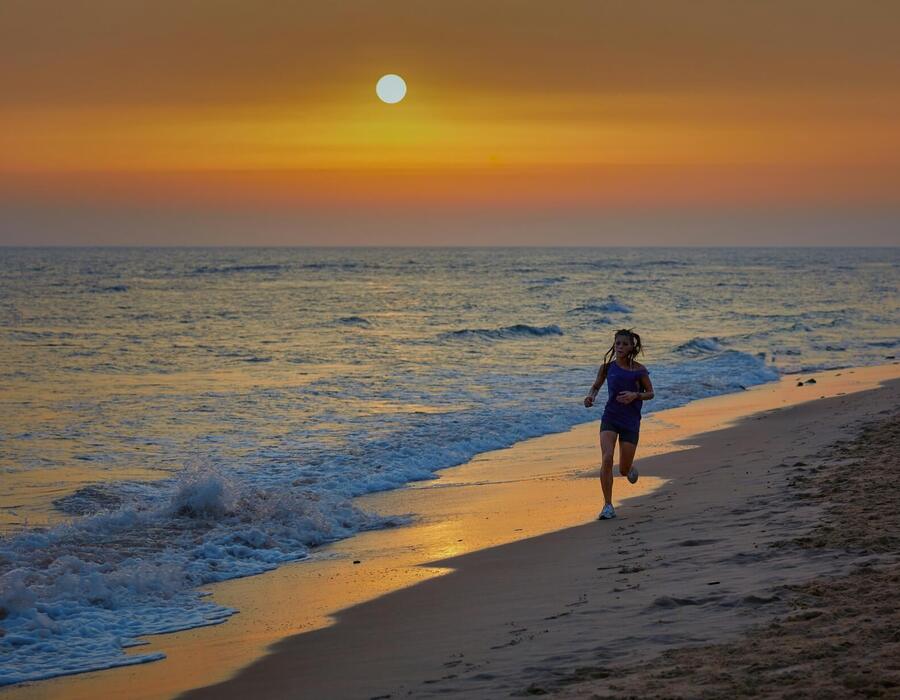 Biegaczka biegnąca brzegiem hotelowej plaży o zachodzie słońca, złote fale myjące piaszczysty brzeg.