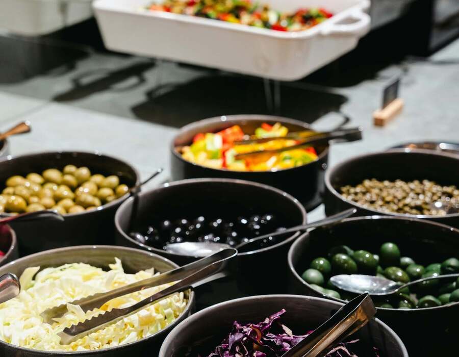 Samodzielny bufet sałatkowy w hotelu: miski z zielonymi i czarnymi oliwkami, białą i fioletową kapustą oraz kolorowymi paprykami.