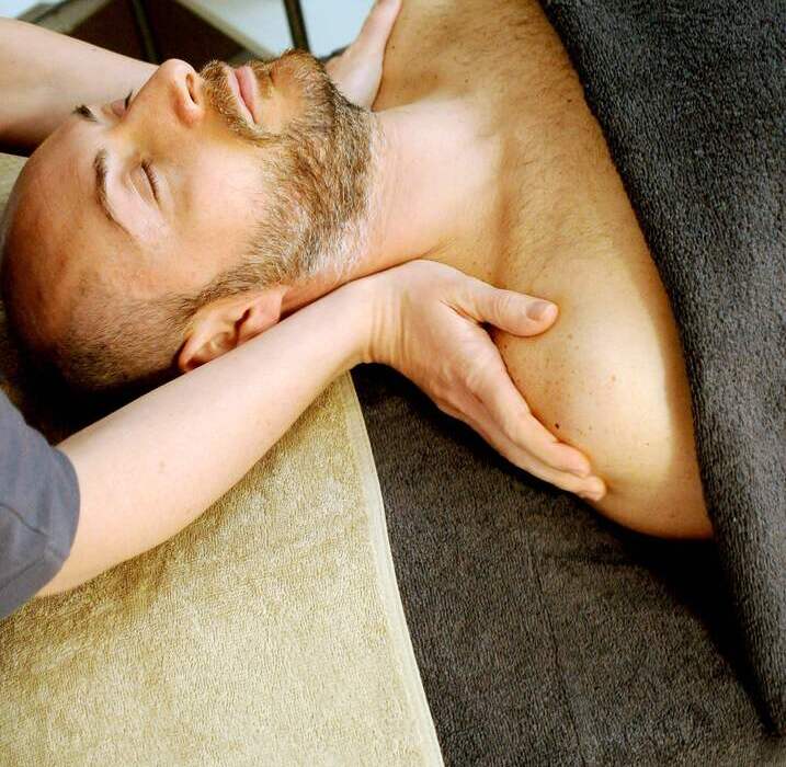 Mężczyzna podczas relaksującego masażu szyi i barków na stole spa, owinięty ręcznikami w spokojnej sali zabiegowej.