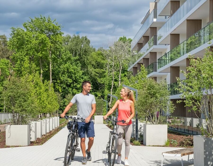 Para prowadzi rowery przy hotelu z nowoczesnymi balkonami, bujną zielenią i leśnym widokiem