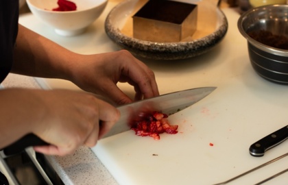 Szef kuchni sieka świeże truskawki na białej desce w hotelowej kuchni, obok form i misek.