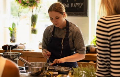 Szef kuchni prowadzi warsztaty kulinarne w jasnej kuchni, przygotowując składniki ze świeżymi ziołami i owocami.