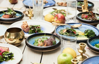 Wspólne degustacyjne dania na niebieskiej ceramice, świeże owoce, kryształowe szklanki i mosiężne świeczniki na stole