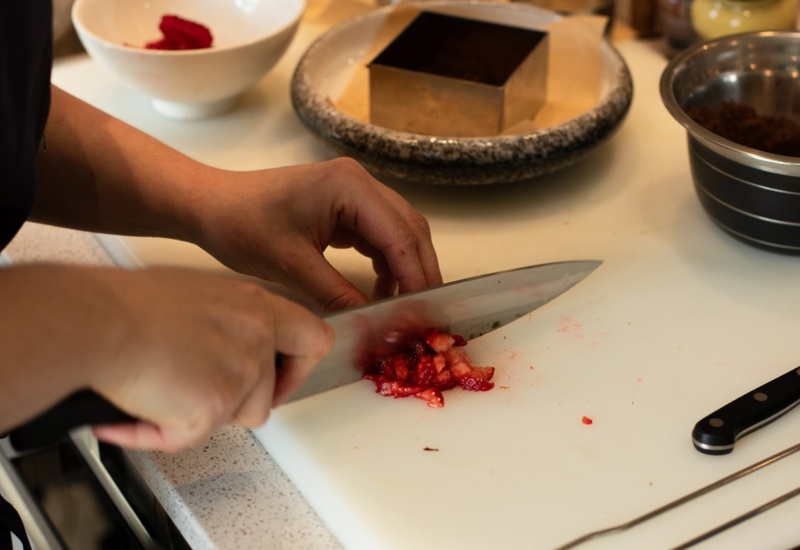 Szef kuchni sieka świeże truskawki na białej desce w hotelowej kuchni, obok form i misek.