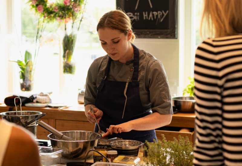 Szef kuchni prowadzi warsztaty kulinarne w jasnej kuchni, przygotowując składniki ze świeżymi ziołami i owocami.