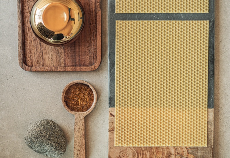 Zestaw spa: dwa plastry wosku pszczelego na drewnianej desce, drewniana łyżka z olejem, gładki kamień i złota miseczka.