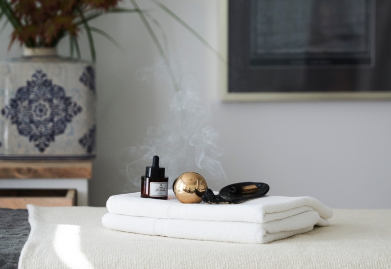 Stół do zabiegów spa z białymi ręcznikami, olejkiem aromaterapeutycznym i unoszącym się dymkiem kadzidła, w spokojnym wnętrzu.