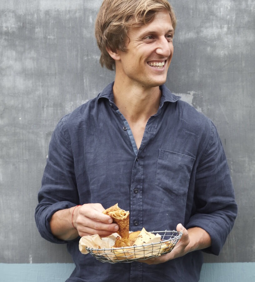 Uśmiechnięty mężczyzna trzyma koszyk ze świeżymi wypiekami, delektuje się porannym śniadaniem w kawiarni hotelowej