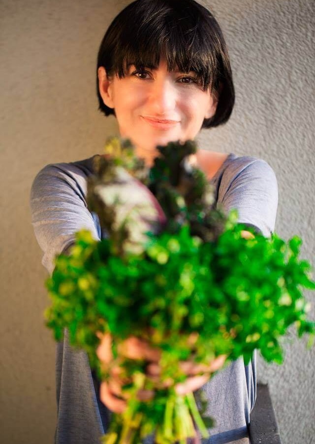 Uśmiechnięta osoba trzyma przed sobą pęk świeżych zielonych ziół, w swobodnej, wewnętrznej scenerii