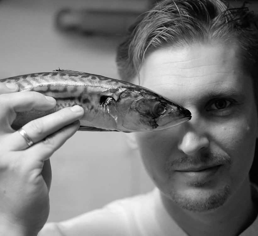 Szef kuchni trzyma świeżą makrelę przy oku w kuchni, prezentując owoce morza w restauracji