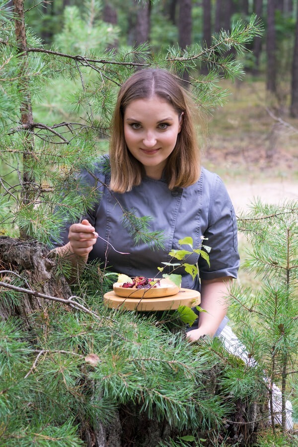 Szefowa kuchni degustuje sezonowe danie na drewnianej desce w sosnowym lesie, rustykalna plenerowa atmosfera