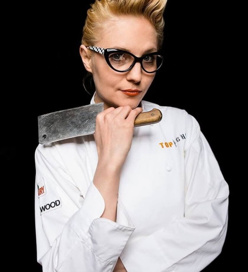 Szefowa kuchni hotelowej w białym kitlu i kocich okularach, trzyma tasak na ramieniu — pewny portret restauracji