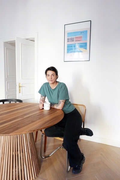 Gość przy okrągłym drewnianym stole z kawą, jasne minimalistyczne wnętrze i oprawiony plakat