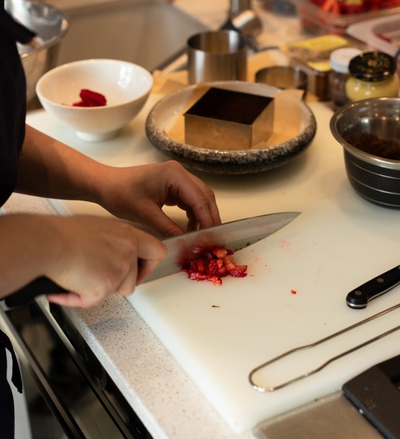 Szef kuchni sieka świeże truskawki na białej desce w hotelowej kuchni, obok form i misek.