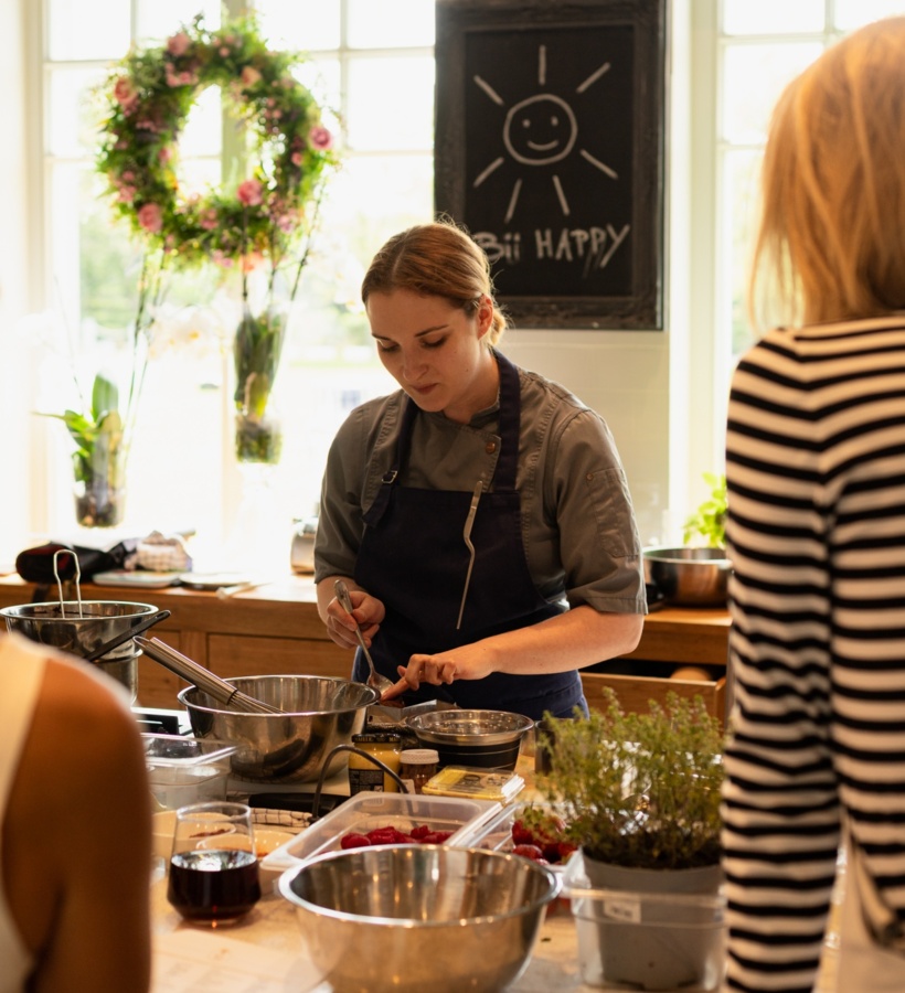 Szef kuchni prowadzi warsztaty kulinarne w jasnej kuchni, przygotowując składniki ze świeżymi ziołami i owocami.