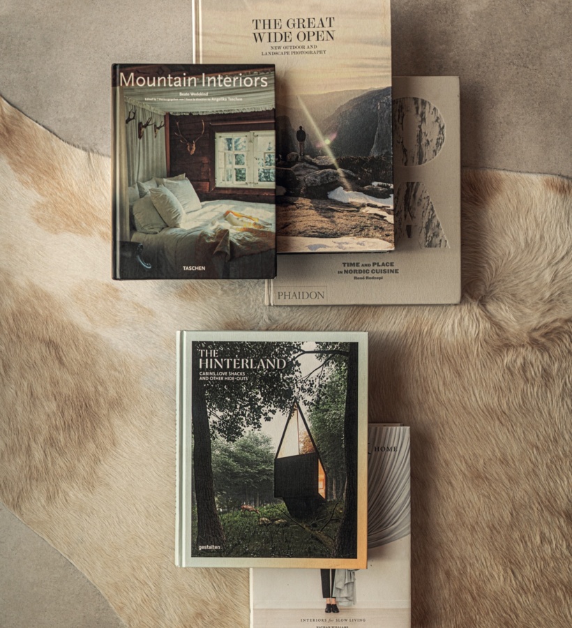 Stos książek o podróżach i wnętrzach na miękkim futrze — przytulny kącik czytelniczy z rustykalnym, nordyckim charakterem.