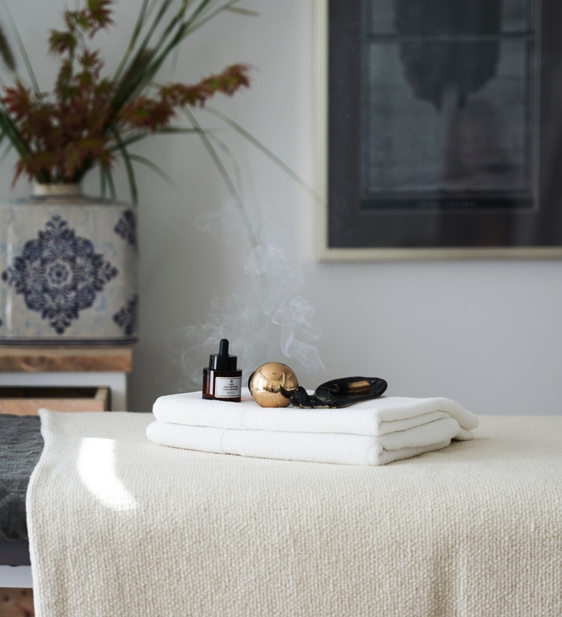 Stół do zabiegów spa z białymi ręcznikami, olejkiem aromaterapeutycznym i unoszącym się dymkiem kadzidła, w spokojnym wnętrzu.