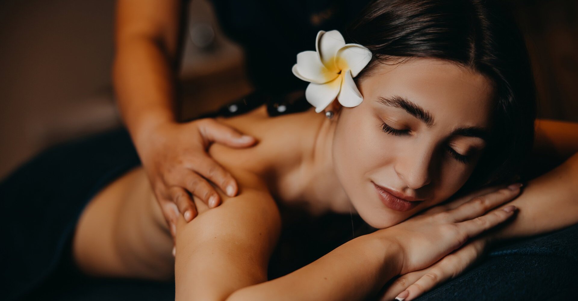 Uvolněná žena s květem ve vlasech dostává masáž zad v klidném hotelovém spa