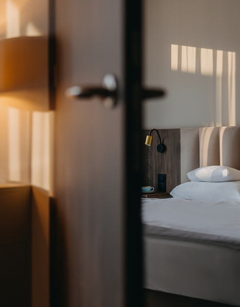 Příjemný hotelový pokoj se dvěma postelemi, bílým povlečením, měkkým čelem postele a teplým světlem stolní lampy.