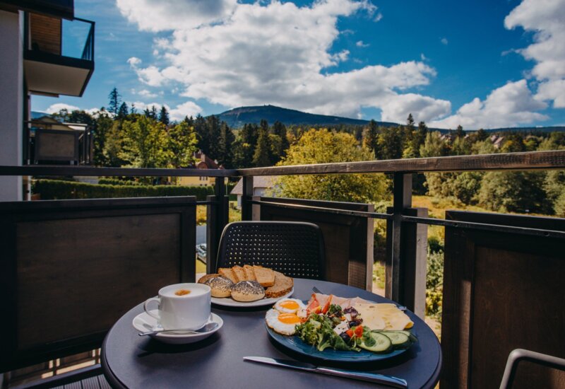 Breakfast on a hotel balcony with mountain views, fresh bread, eggs, cheese, salad, and coffee served on a table