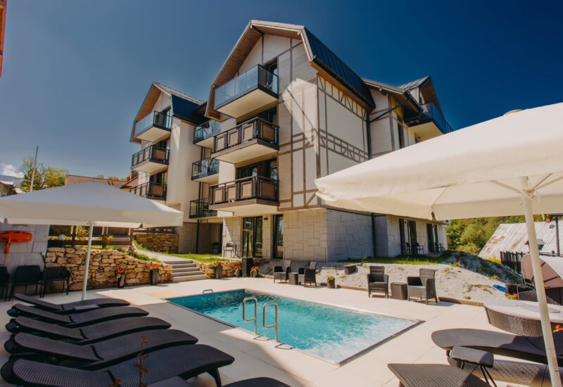 Modern hotel with wooden balconies and heated outdoor pool surrounded by lounge chairs and umbrellas