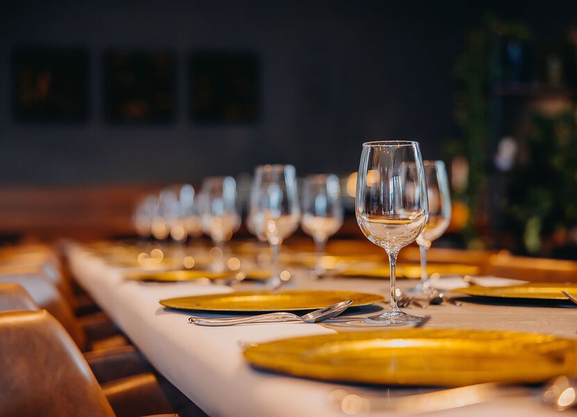 Elegancko nakryty stół z białym obrusem, złotymi talerzami i kryształowymi kieliszkami w przytulnej restauracji.